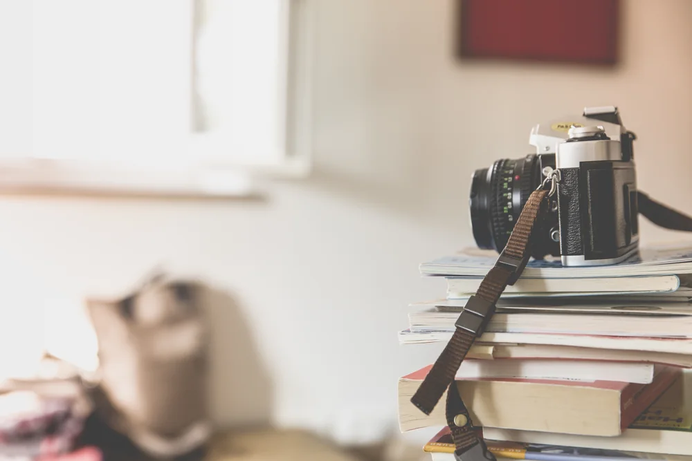 Un appareil photo argentique posé sur une pile de livres et de magazines.