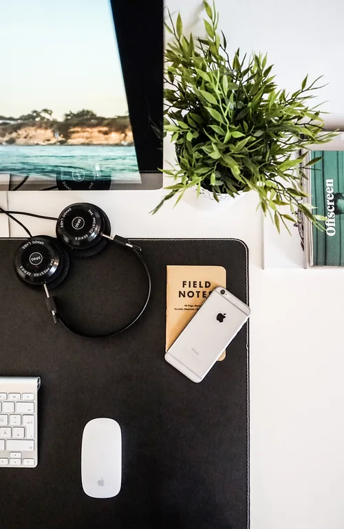 Un carnet, un téléphone et un casque audio disposés sur un bureau près d’un écran.